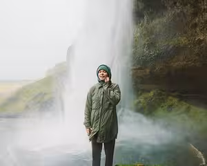 Traveler standing before Seljalandsfoss waterfall on Iceland's misty south coast