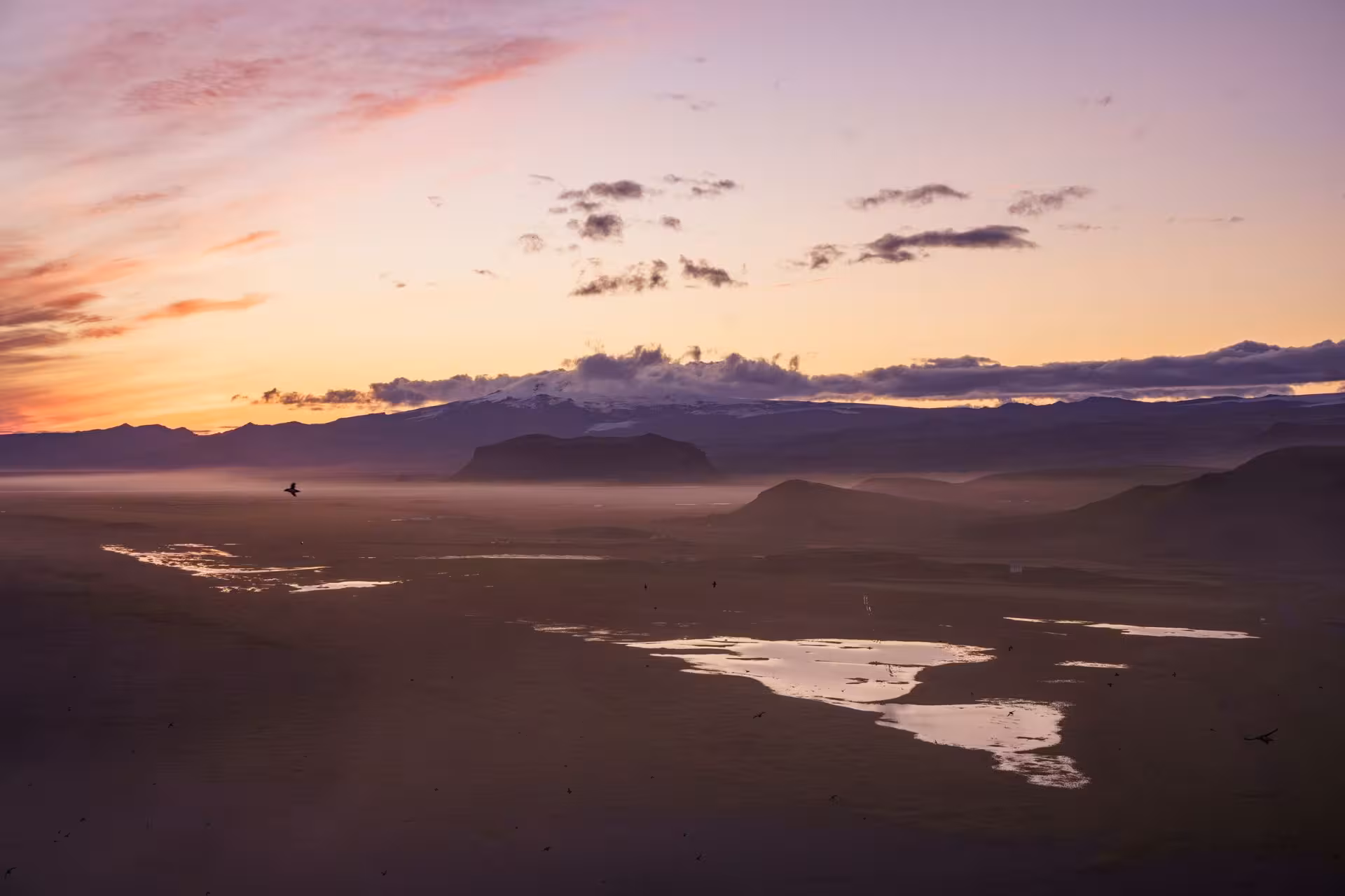 Aerial view of Iceland's south coast at sunset with glaciers, misty plains, and reflective river channels