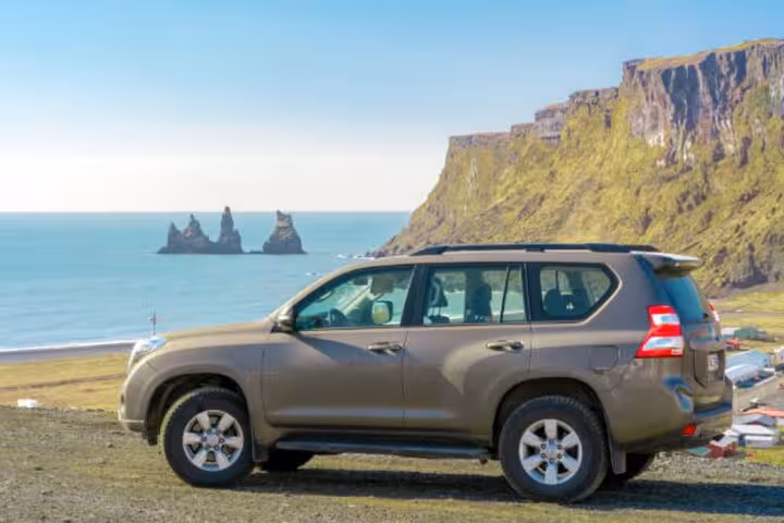 Toyota Land Cruiser SUV parked on Iceland's South Coast with black sand beach and sea stacks in background