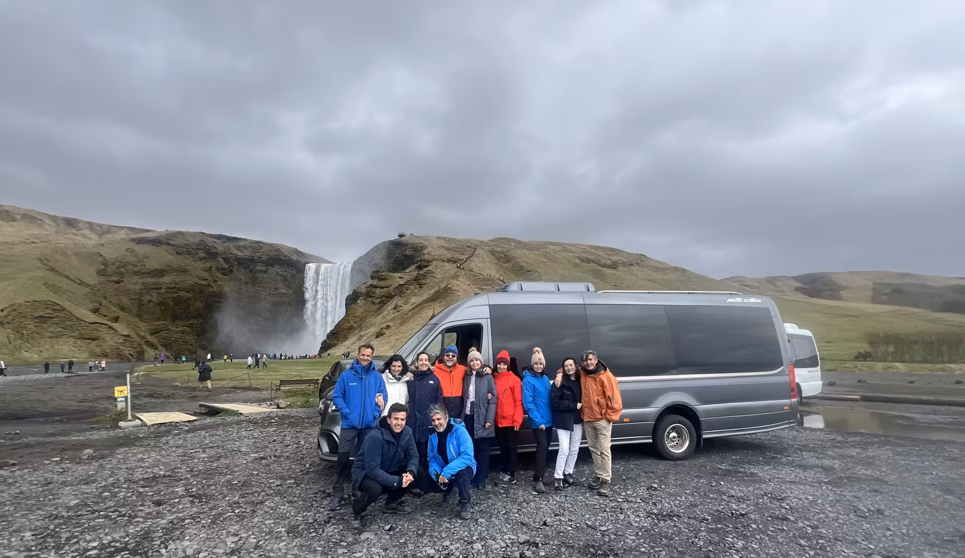 Tour group posing in front of minibus at Skógafoss waterfall on Iceland South Coast full-day tour