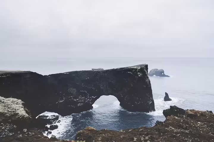 Black volcanic rock arch over ocean on Iceland's south coast with misty sea stacks in background