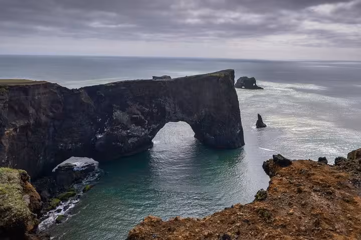 Black volcanic rock arch over turquoise ocean on Iceland's South Coast with sea stacks in background