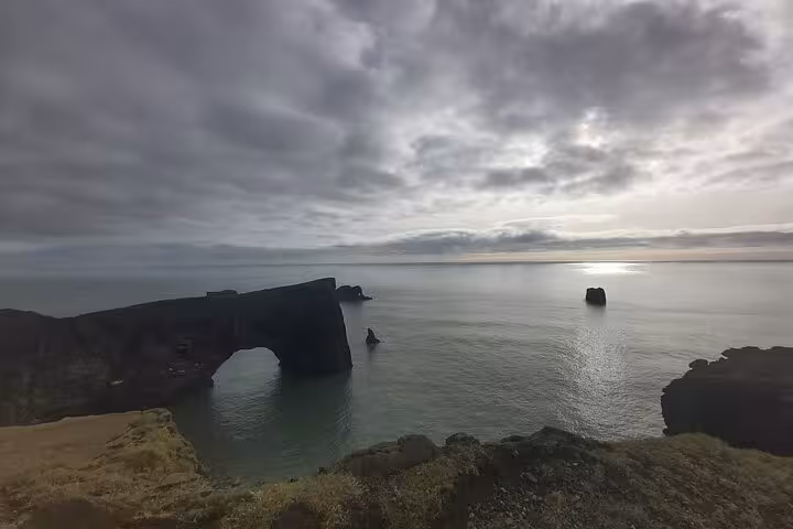 Rocky sea arch on Iceland's south coast with calm ocean waters under dramatic cloudy sky