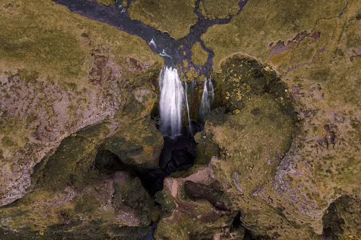 Aerial view of a waterfall cascading through mossy volcanic rocks in Iceland's south coast