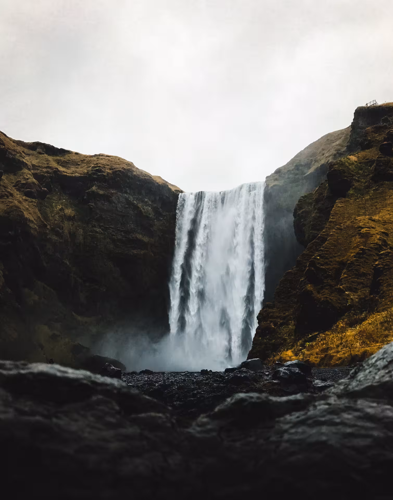 Powerful Skógafoss waterfall cascading down dark cliffs on Iceland's south coast under overcast skies