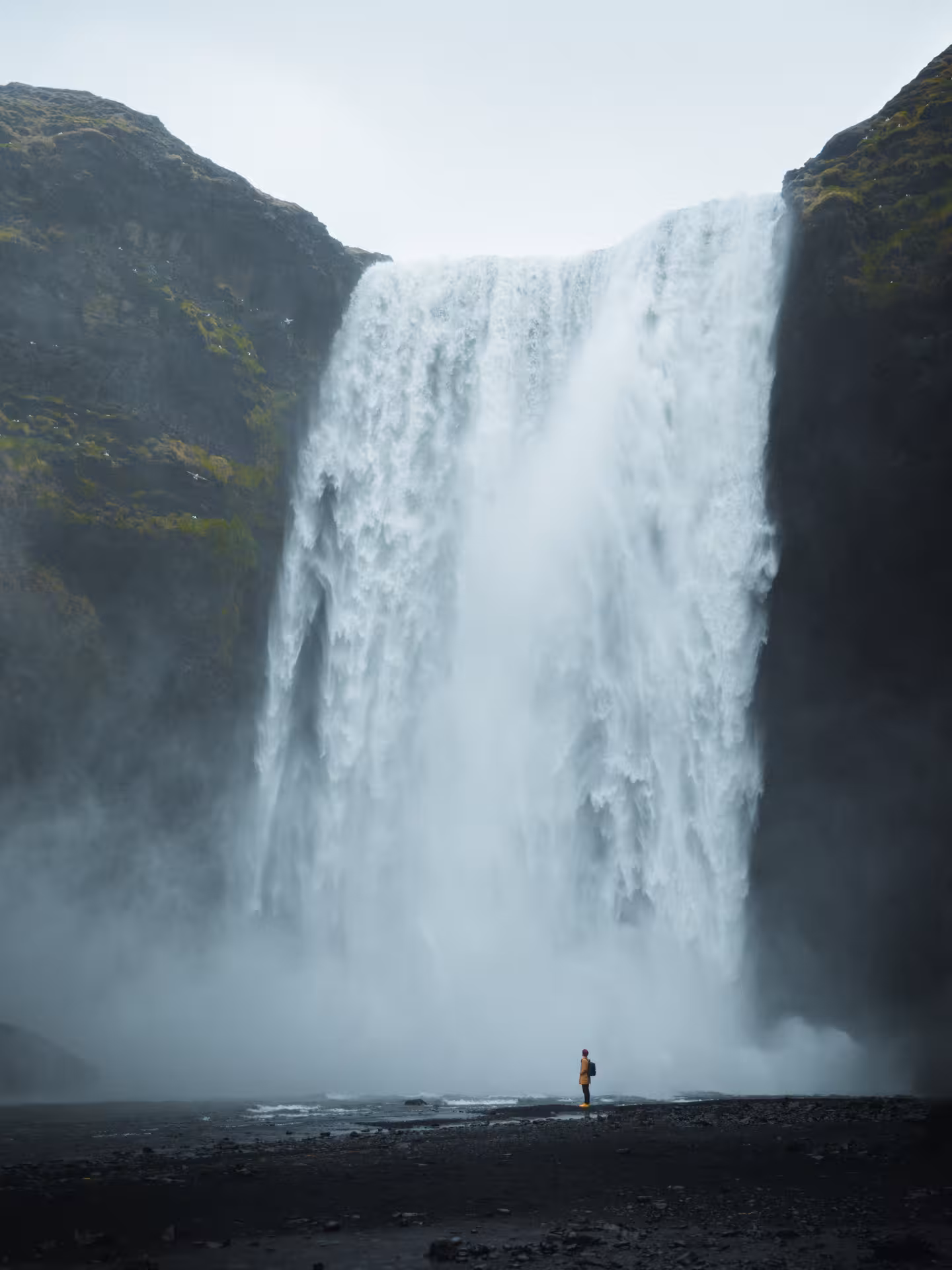 Lone traveler standing before massive Skógafoss waterfall on Iceland's south coast surrounded by mist
