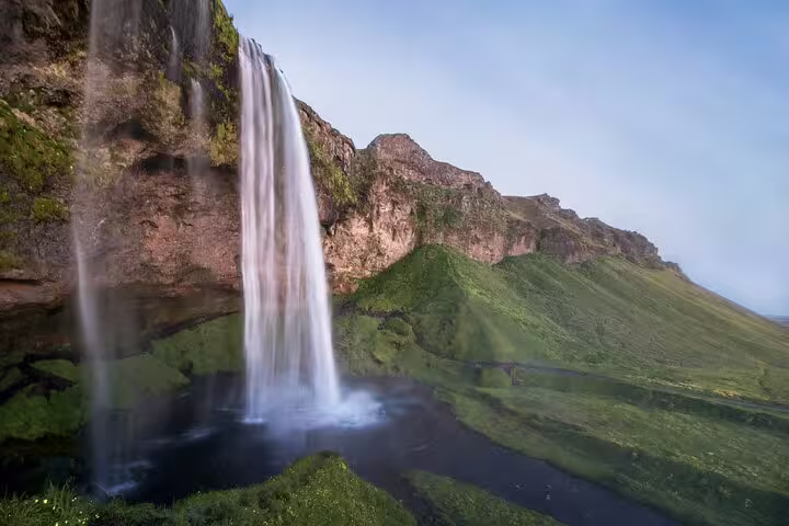 Tall waterfall cascading down mossy cliffs on Iceland's South Coast with green hillside backdrop