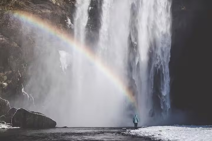 Person standing before massive Skógafoss waterfall with rainbow arc in Iceland