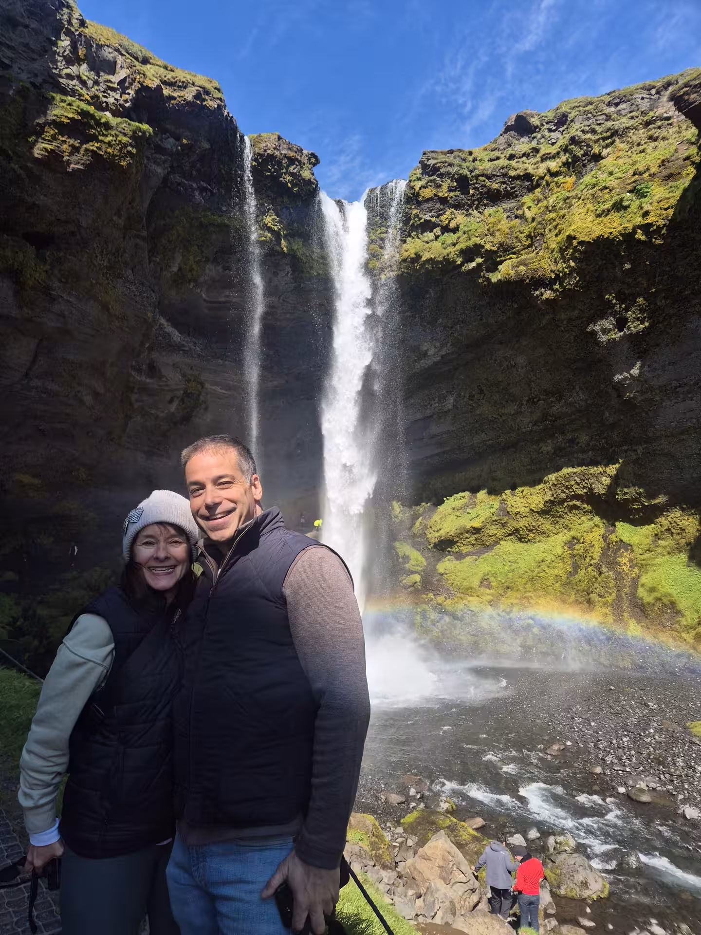 Couple smiling in front of Kvernufoss waterfall with rainbow on Iceland South Coast tour