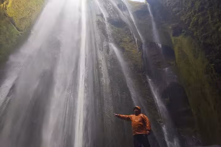 Person in orange jacket standing behind massive waterfall on Iceland South Coast tour