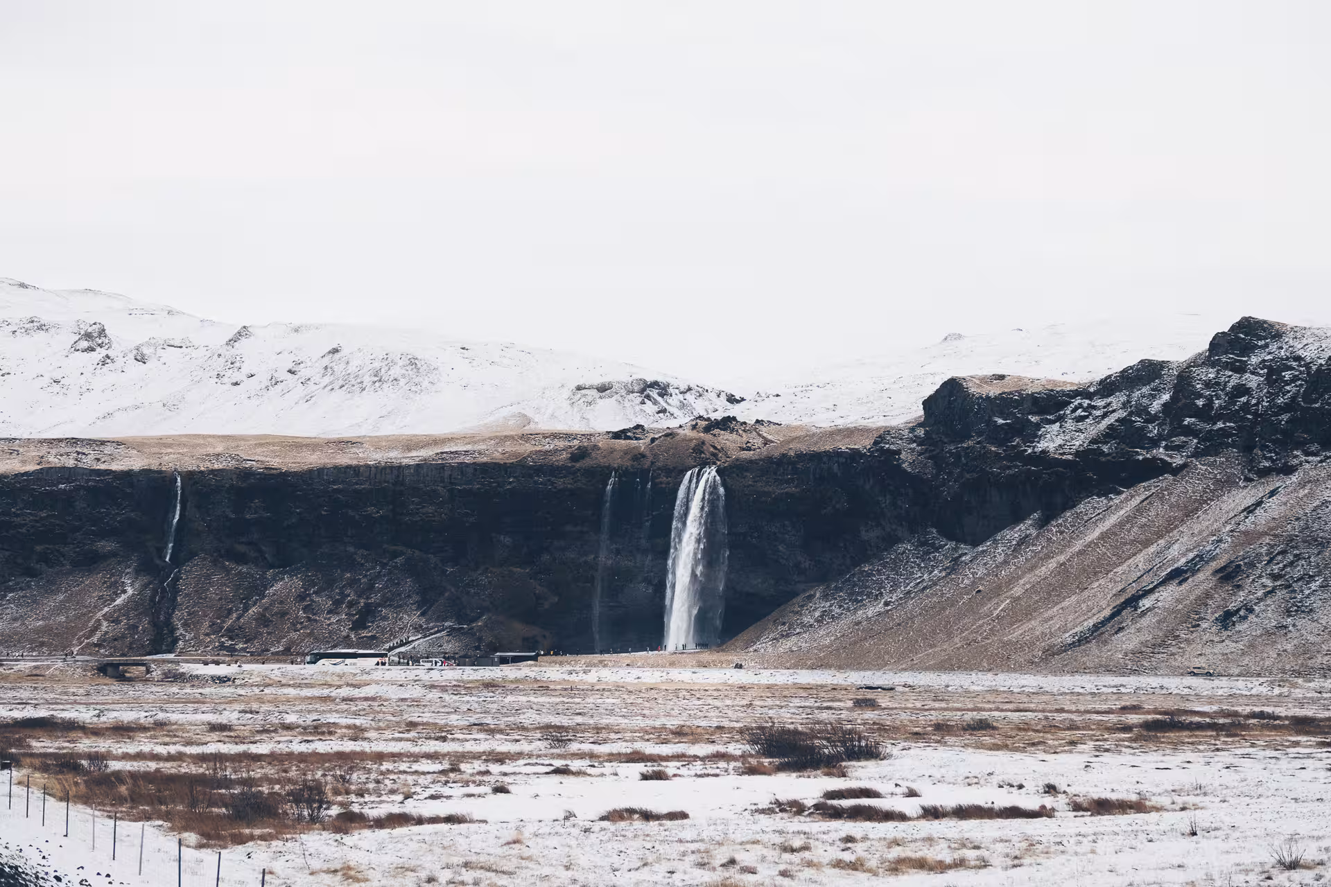 Seljalandsfoss waterfall cascading down cliffs in snowy Iceland winter landscape with mountains