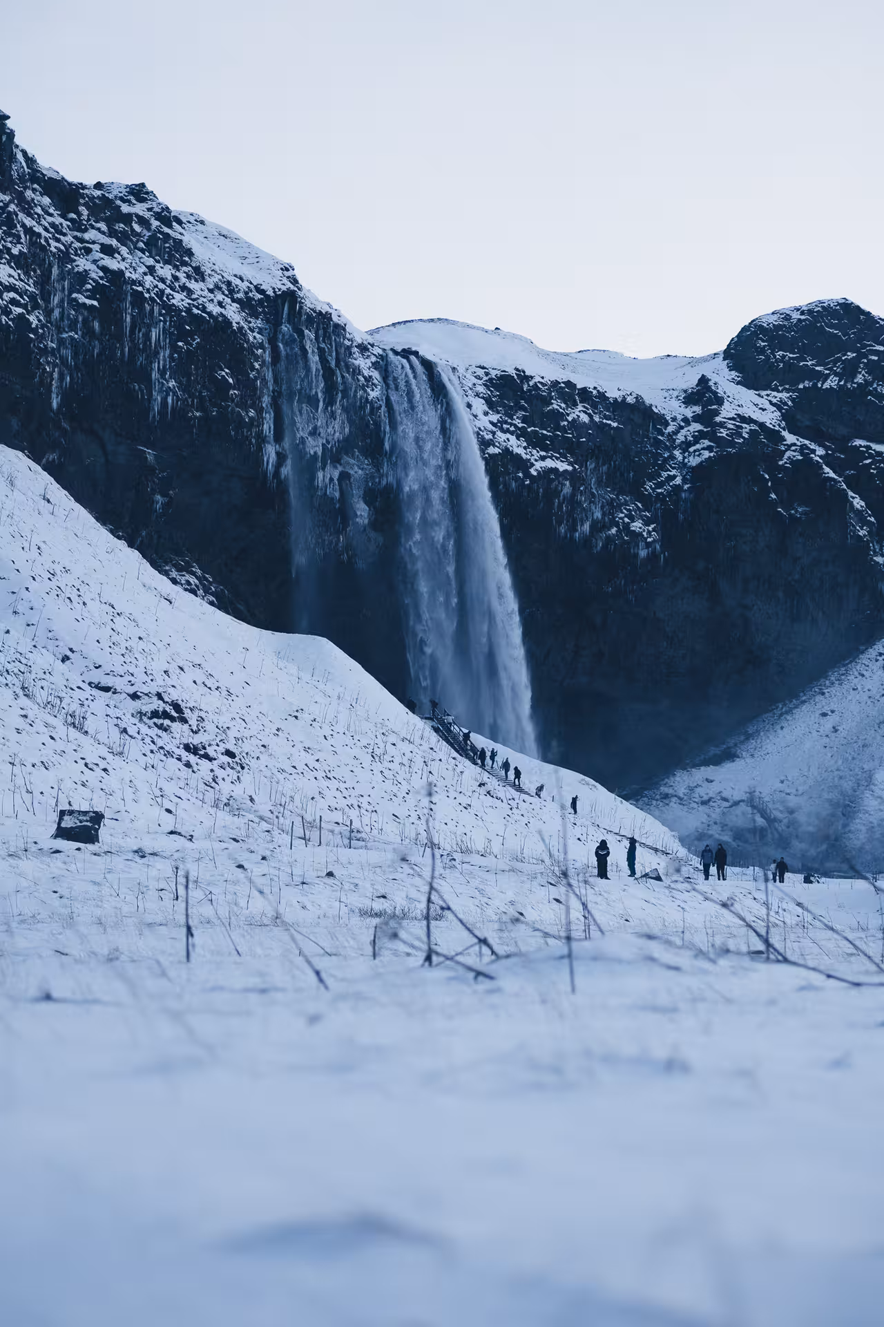 Skógafoss waterfall in winter with visitors hiking snowy slope on Iceland's south coast