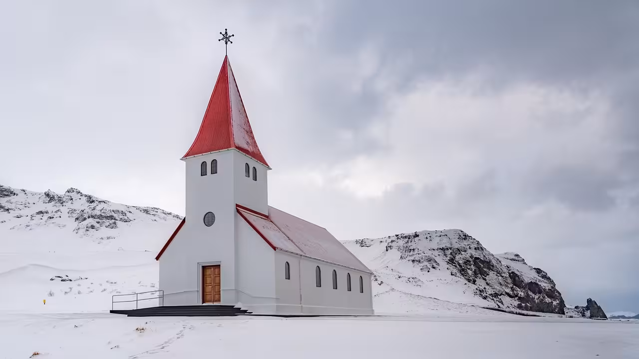 White church with red roof and cross surrounded by snow-covered mountains on Iceland's South Coast