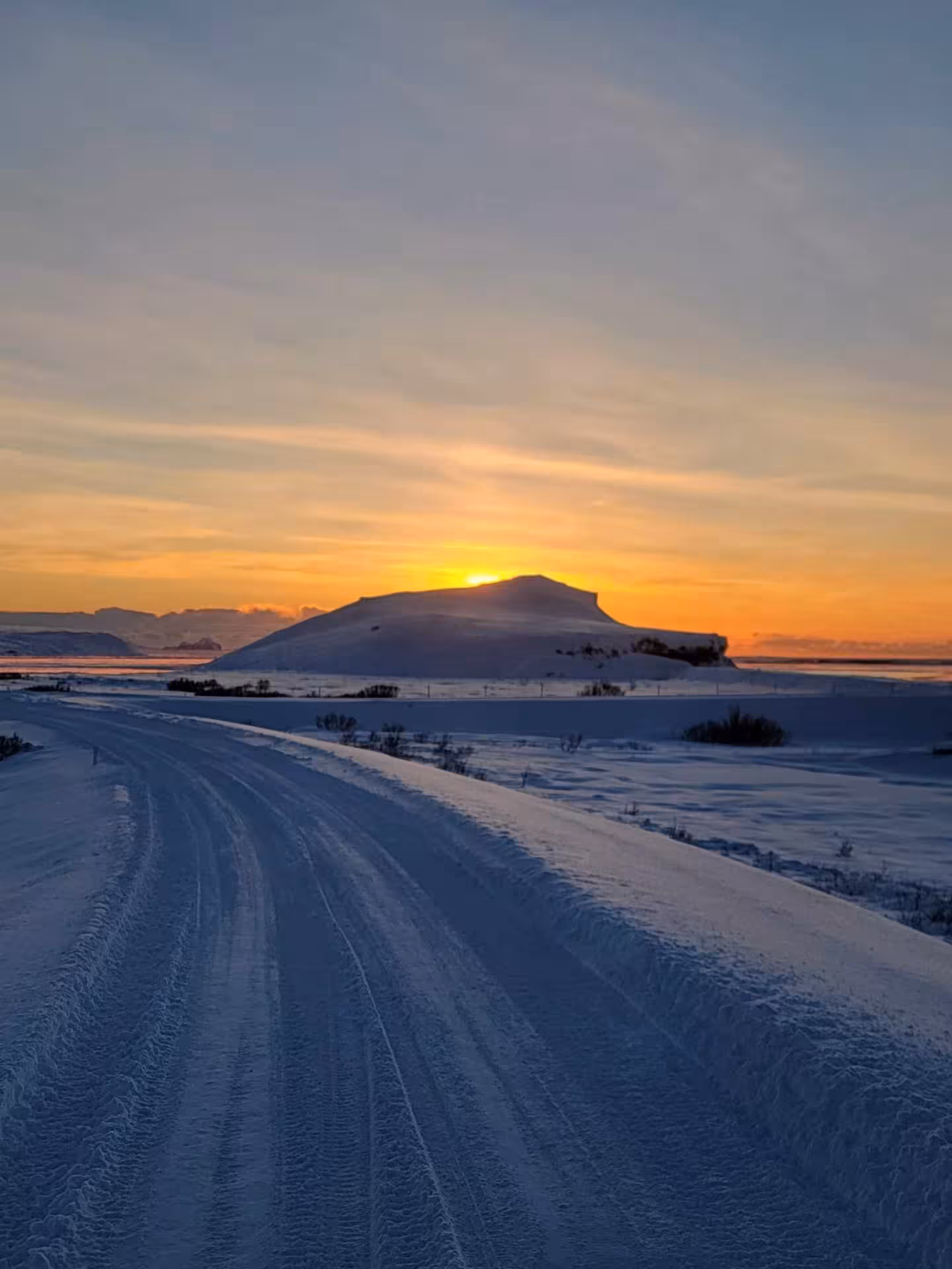 Snow-covered road leading toward a volcanic hill silhouetted against a golden sunset in Iceland