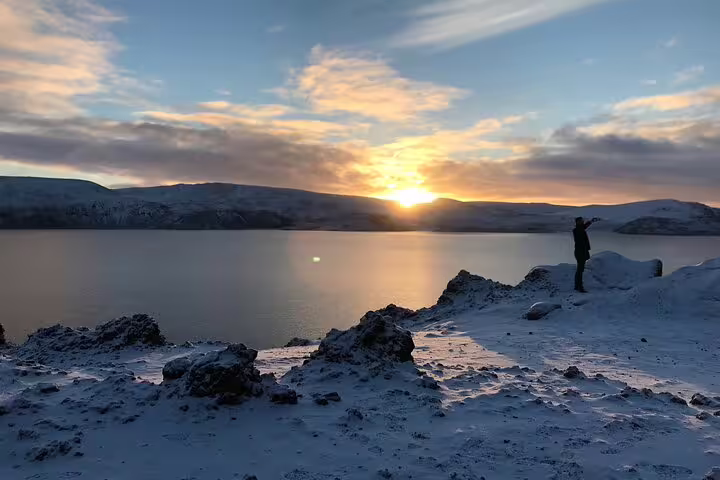 Silhouette of person standing on snowy lakeshore at sunset in Iceland with mountains in background