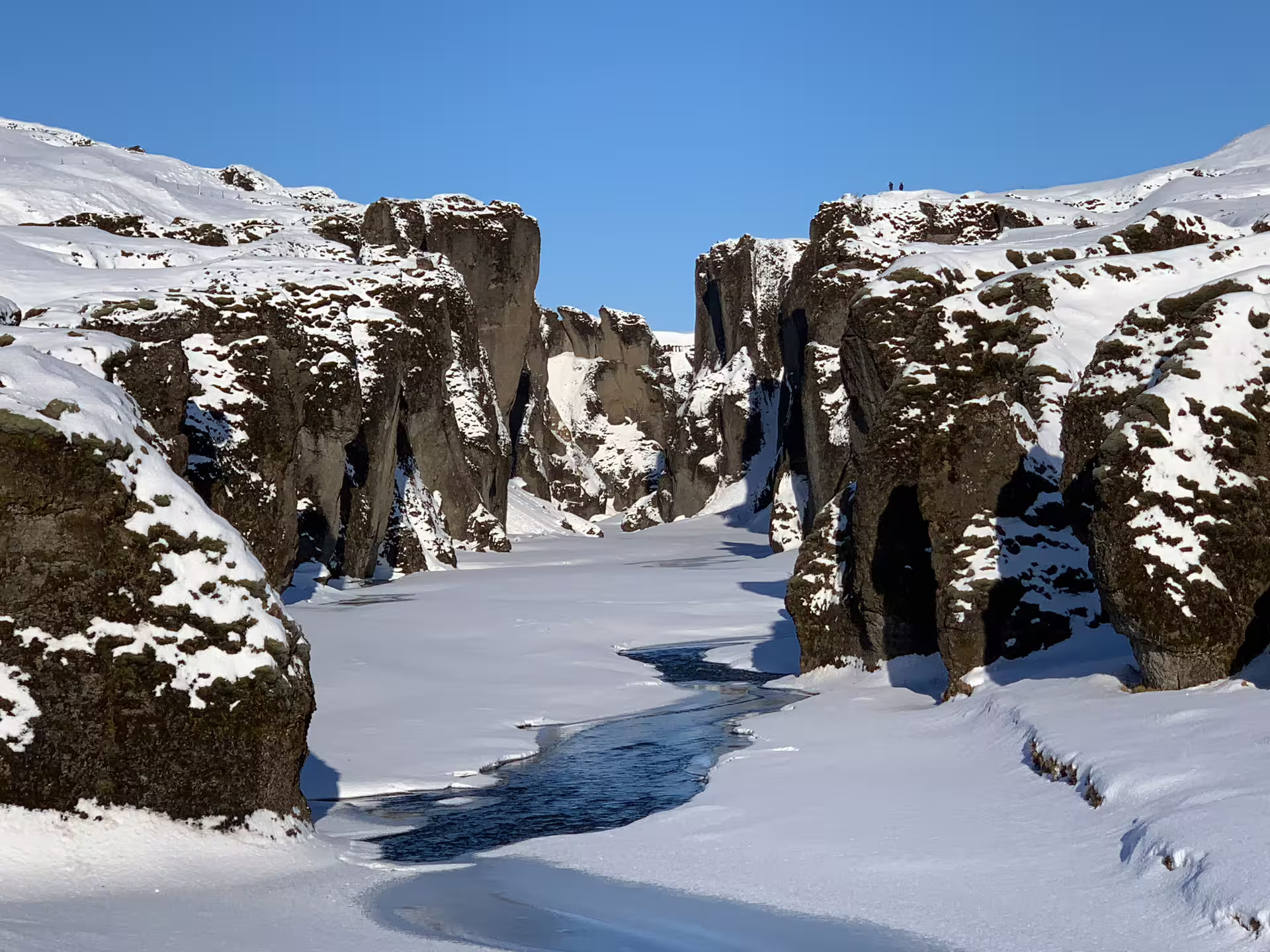 Snow-covered Fjaðrárgljúfur canyon with frozen river winding through towering basalt rock walls in Iceland winter