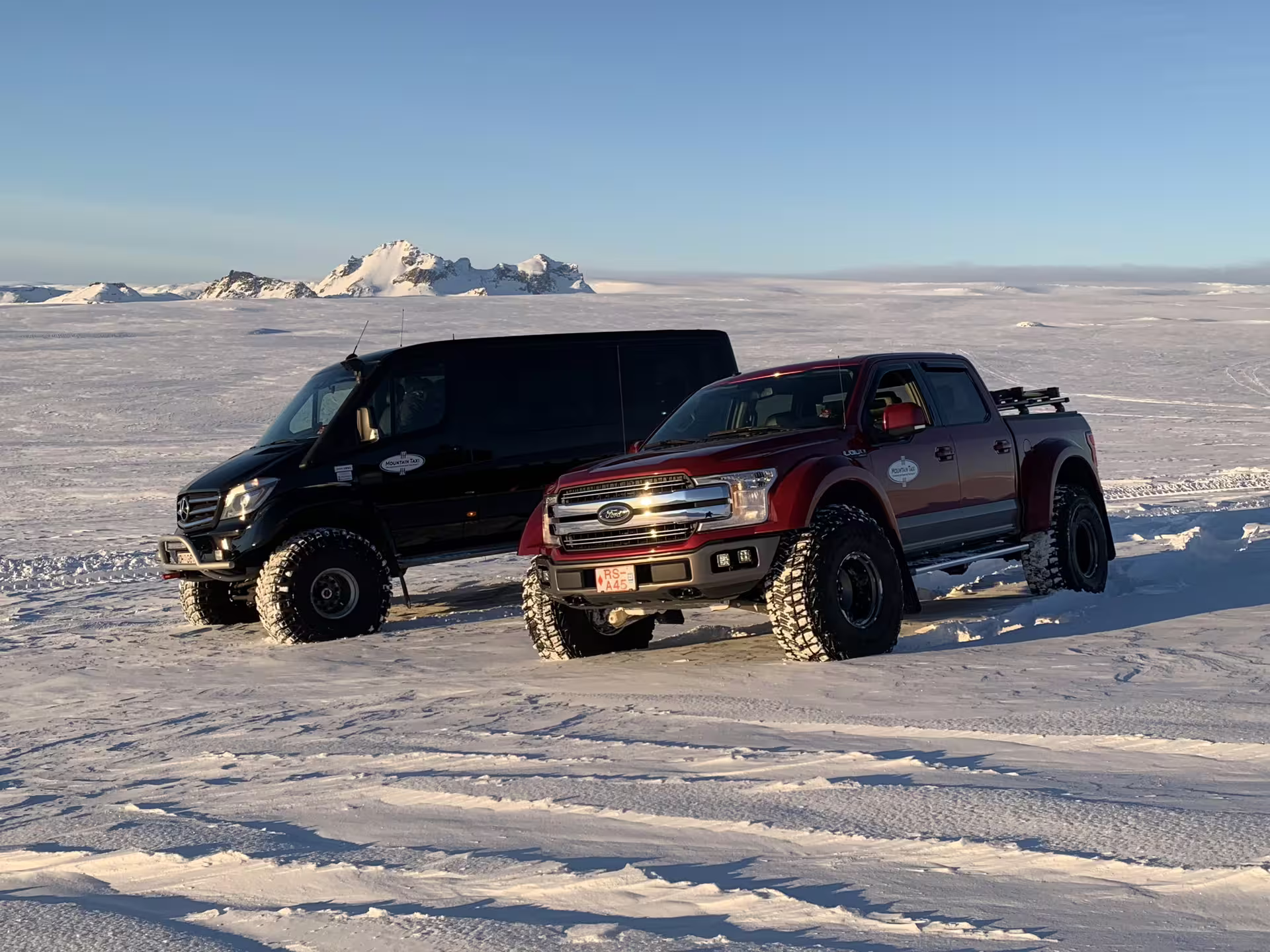 Red Ford F-150 super jeep and black Mercedes Sprinter 4x4 on Icelandic glacier snowfield