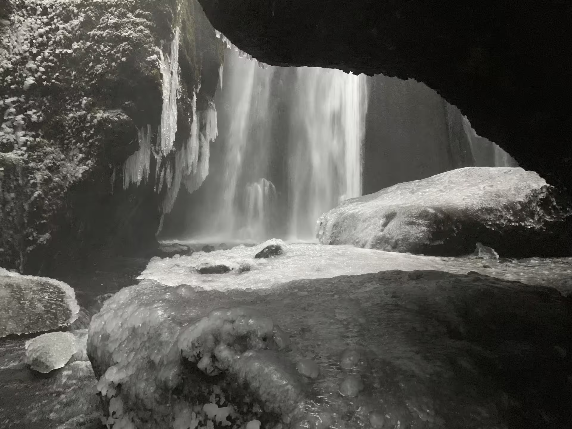 View from behind a frozen waterfall with icicles and snow-covered rocks in Iceland winter landscape