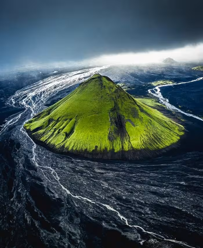 Aerial view of moss-covered volcanic mountain with glacial rivers on black lava fields in Iceland