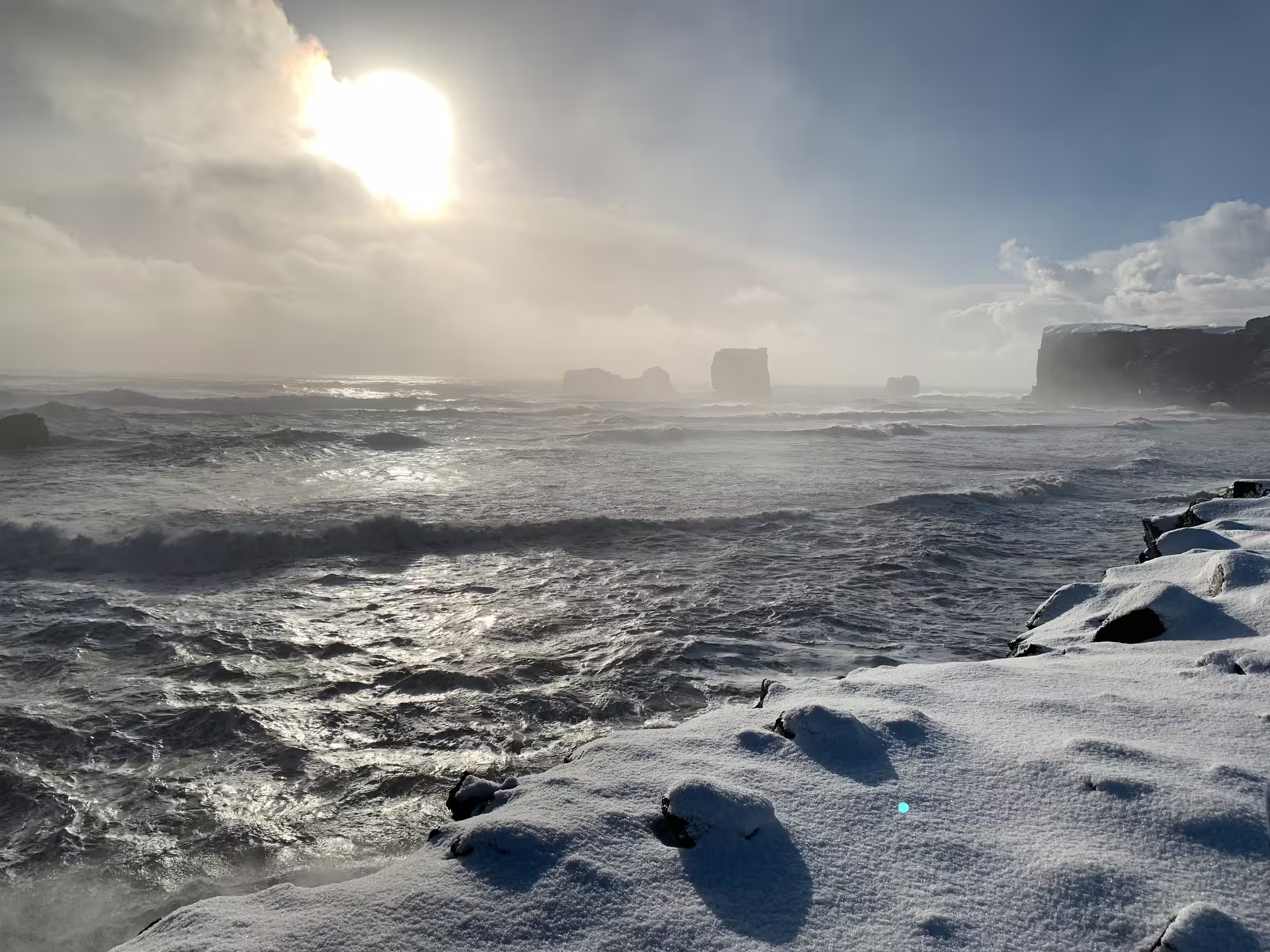 Stormy winter coastline with snow-covered rocks, sea stacks, and rough waves in Iceland