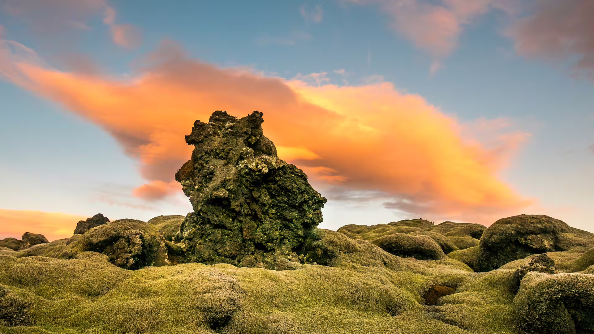 Moss-covered lava fields with a rugged volcanic rock formation under a vivid orange sunset sky in Iceland