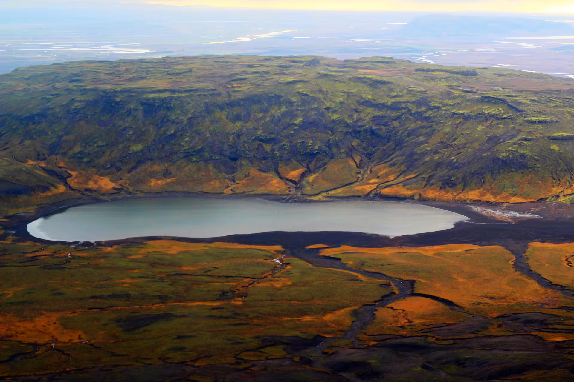 Aerial view of a volcanic crater lake with black sand shores and green mossy cliffs in Iceland