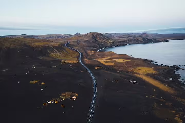 Aerial view of winding road through Iceland's black lava landscape with mountains and coastal waters