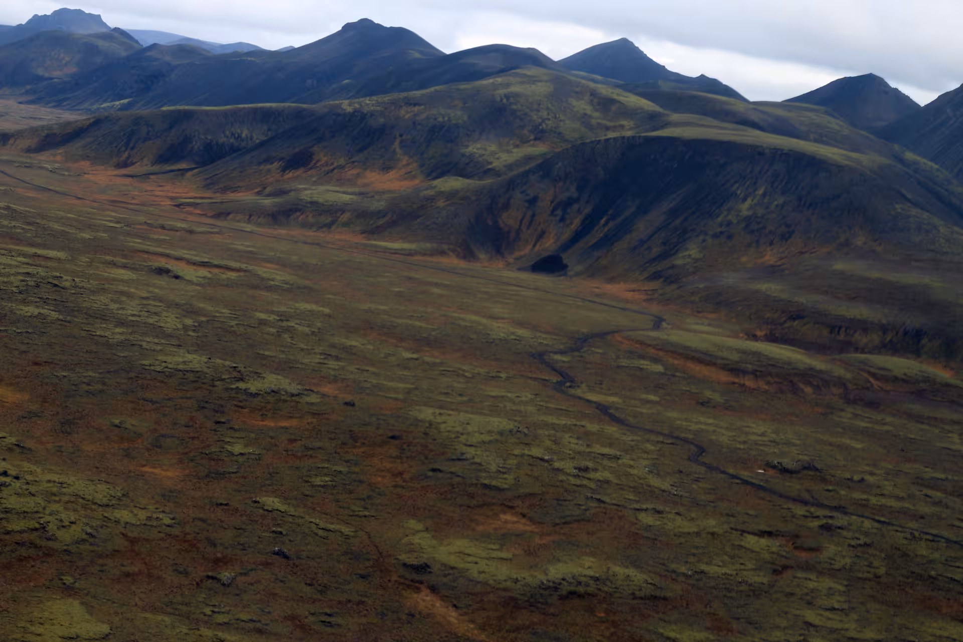 Aerial view of green tundra valley with winding stream and dark volcanic mountains in Iceland