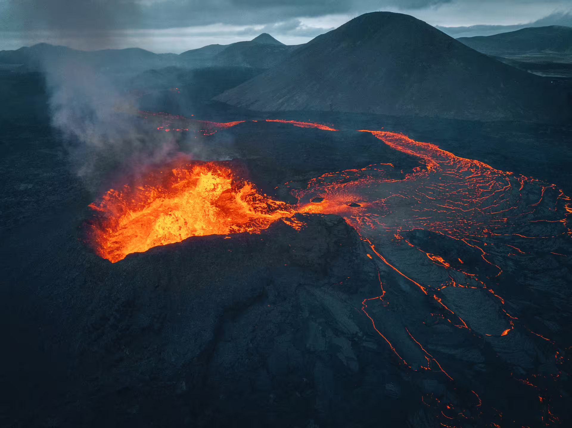 Aerial view of active volcano eruption with glowing orange lava flows across dark volcanic landscape in Iceland