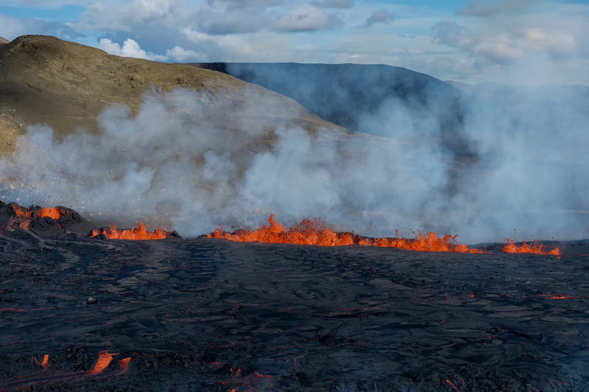 Active lava fissure eruption with glowing orange lava and volcanic smoke on black lava field in Iceland