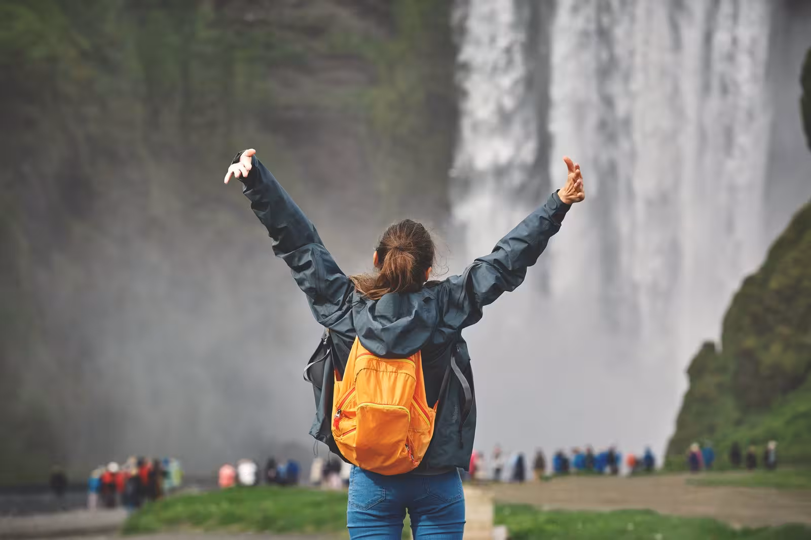 Traveler with arms raised in excitement in front of a majestic waterfall, embracing the adventure of Iceland's natural wonders.