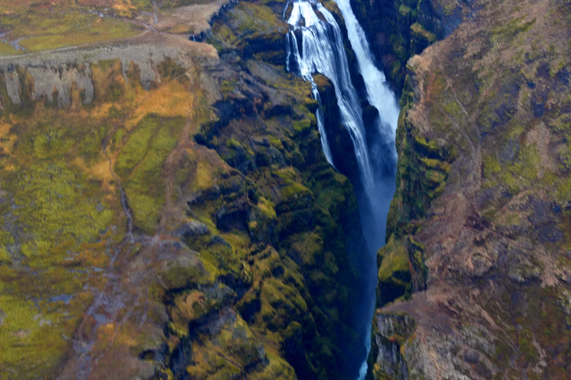 Aerial view of a tall waterfall cascading into a narrow mossy canyon in Iceland
