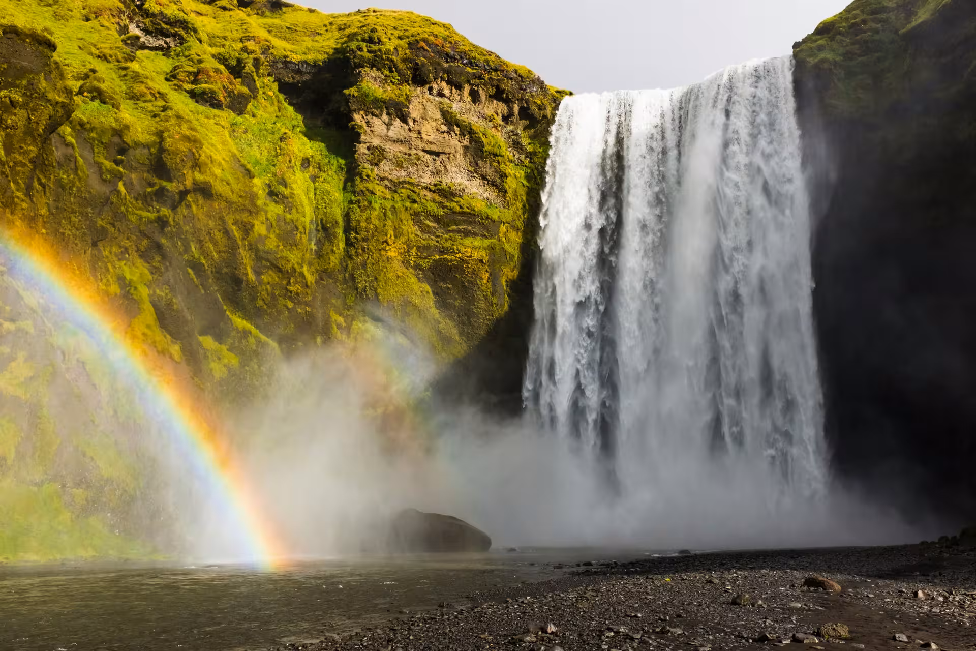 Massive waterfall with double rainbow and moss-covered cliffs in Iceland