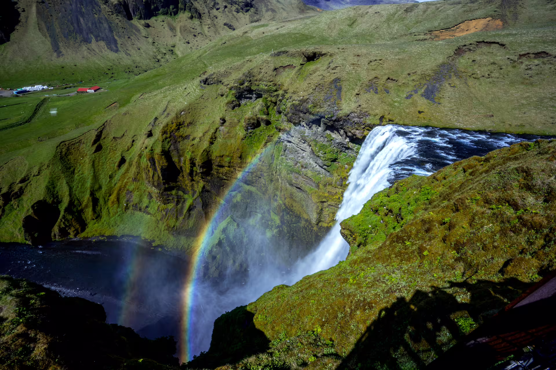 Rainbow forming in mist below Skógafoss waterfall surrounded by green cliffs in Iceland