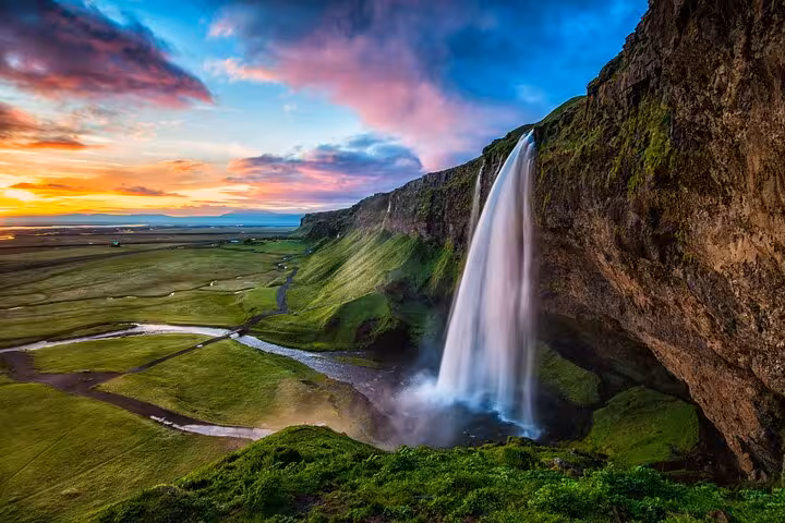 Seljalandsfoss waterfall cascading over green cliffs at sunset in Iceland with winding river below