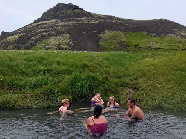 Group of five people relaxing in a natural hot spring pool surrounded by lush green hills in Iceland