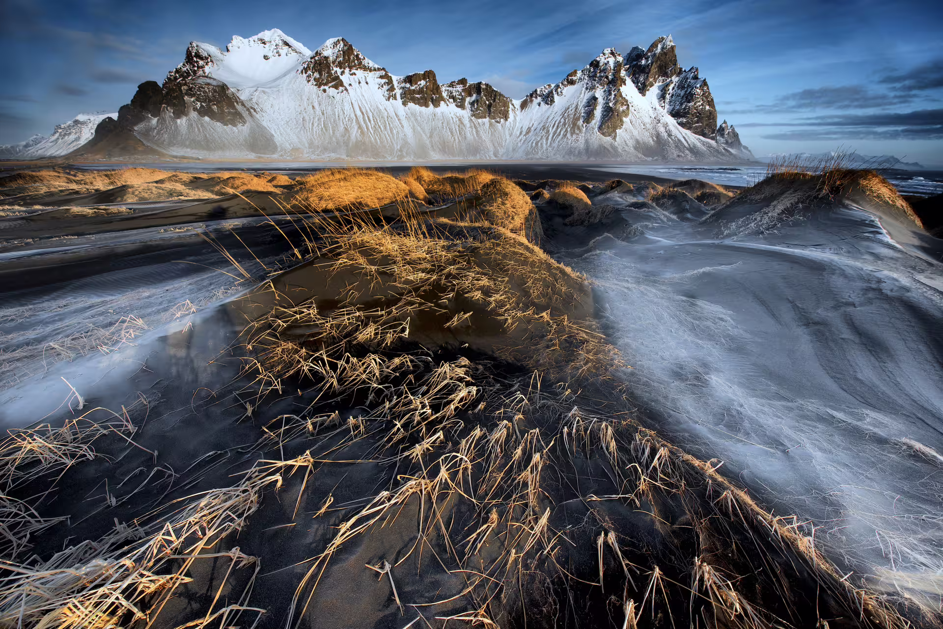Black sand dunes with golden grass and snow-capped Vestrahorn mountain peaks in Iceland winter landscape