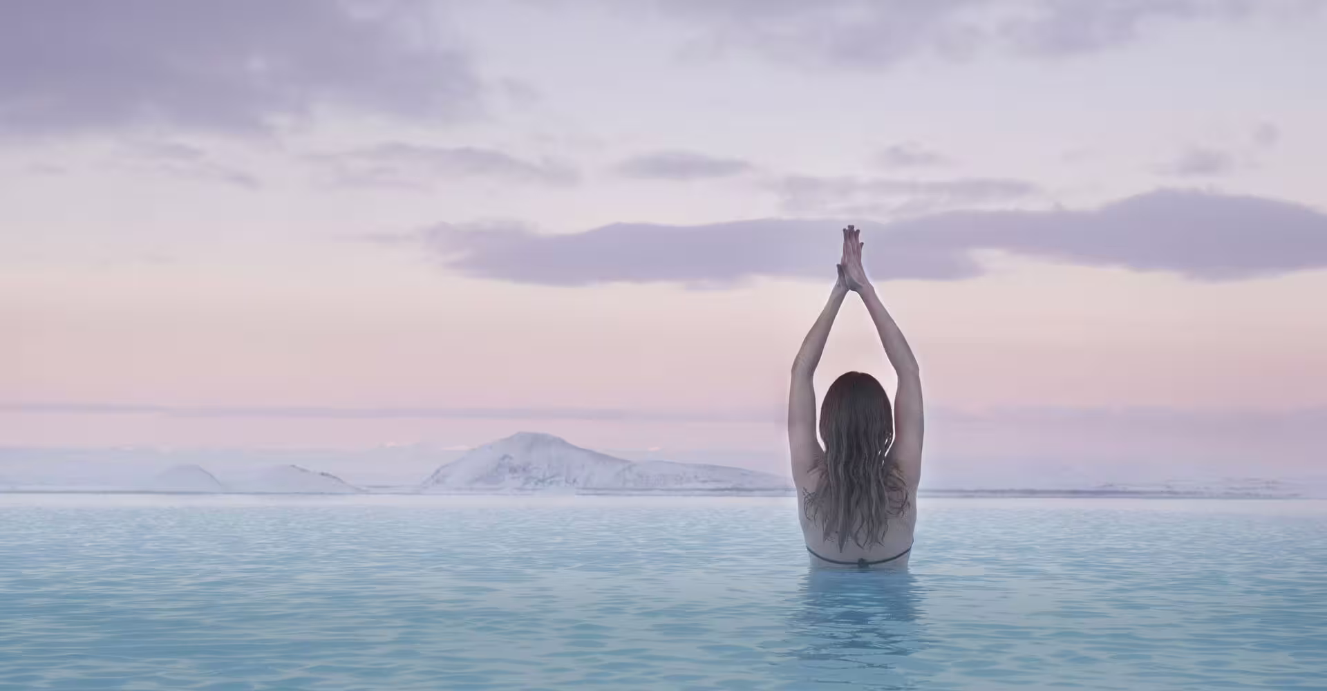 Woman meditating in geothermal infinity pool with snow-capped Icelandic mountains at sunset