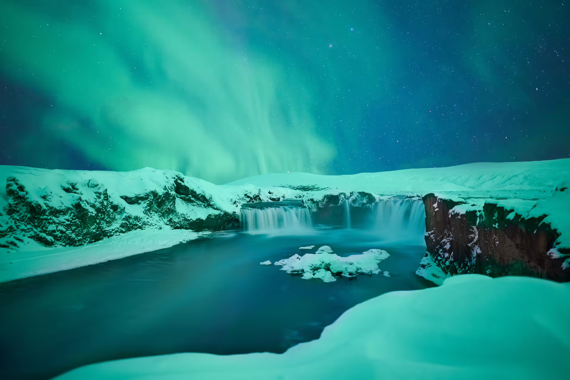 Northern lights over a snow-covered Icelandic waterfall at night with starry sky