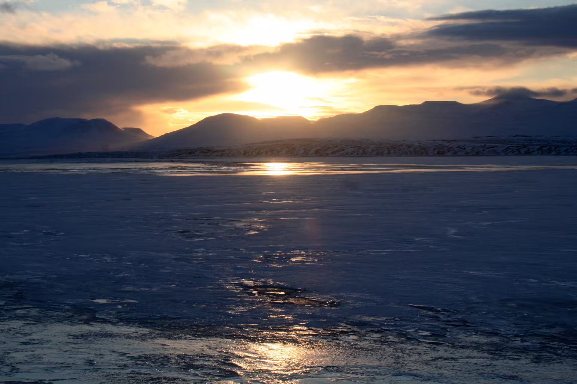 Frozen lake reflecting golden sunset over snow-capped mountains in Iceland during winter