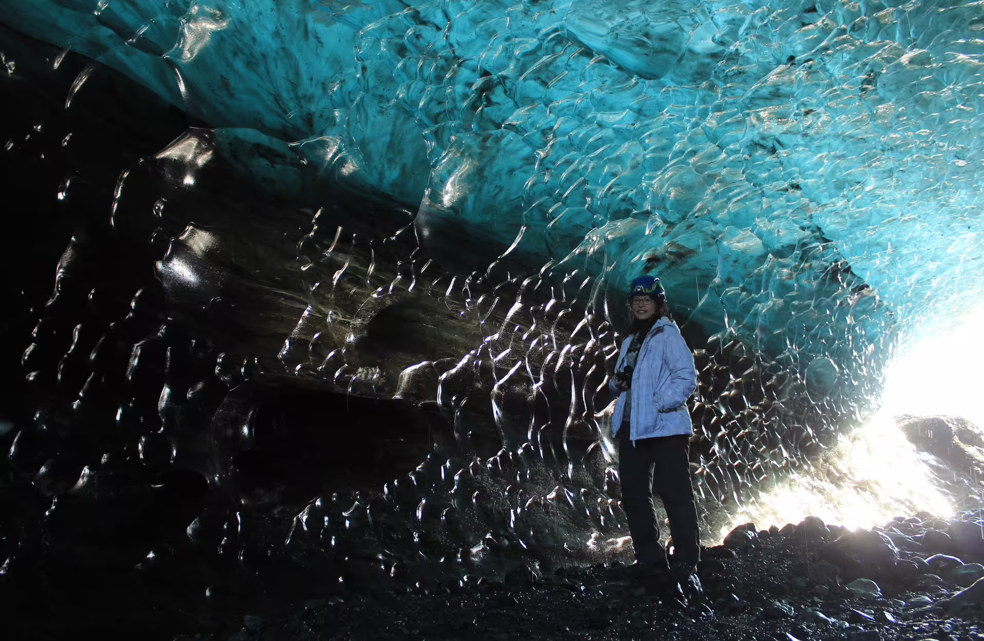 Tourist standing inside a stunning blue glacial ice cave in Iceland with textured ice walls and ceiling