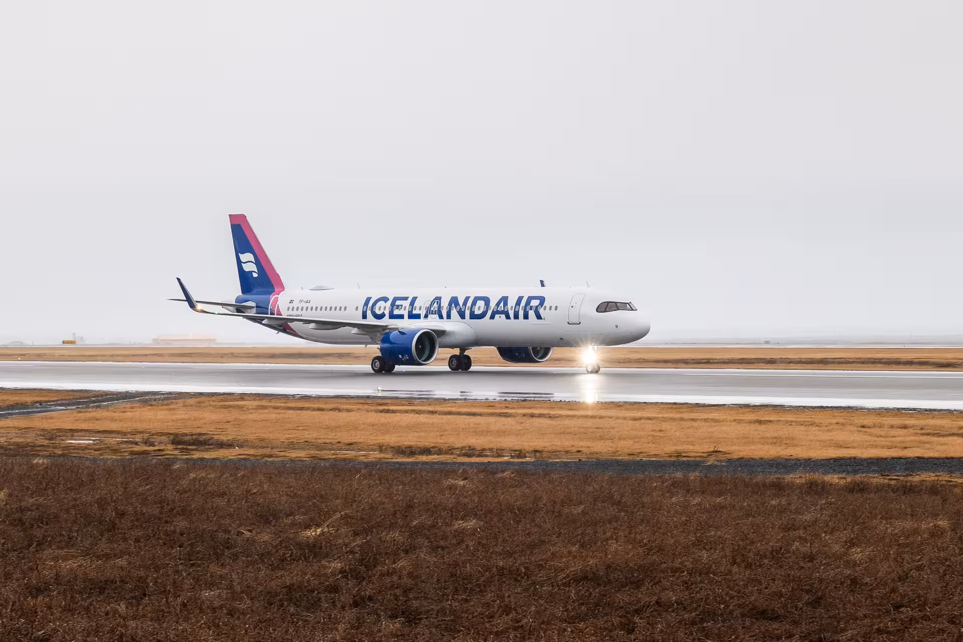 Icelandair aircraft taxiing on wet runway at Keflavik Airport on overcast day