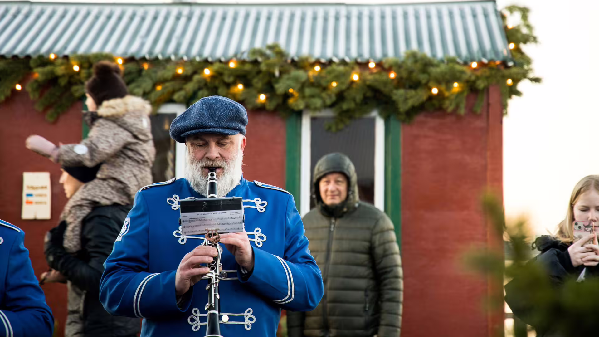 Bearded musician in blue band uniform playing clarinet at Icelandic Christmas market with festive lights