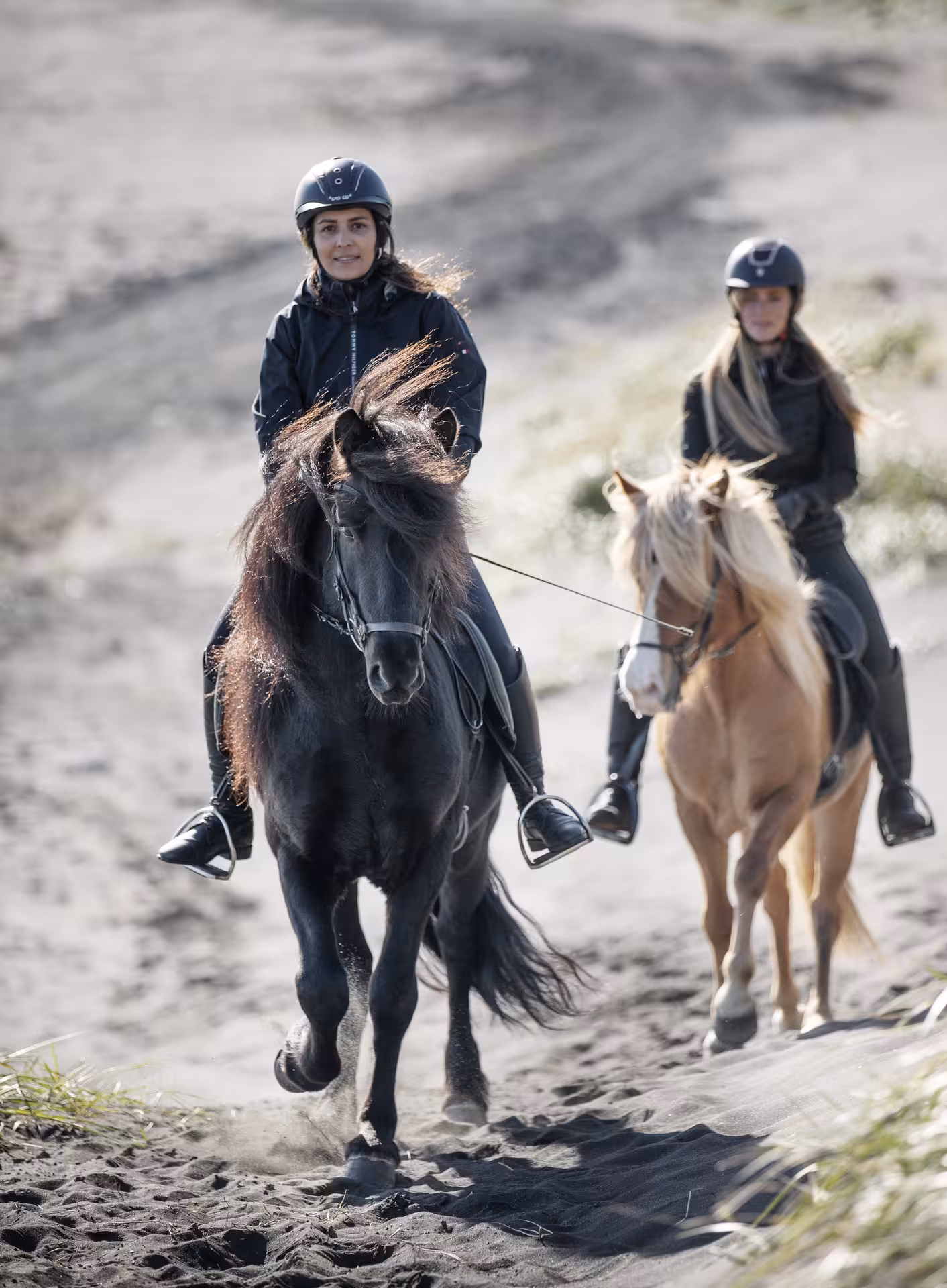 Two riders on Icelandic horses trekking over black sand dunes on a 2-hour private horseback riding tour