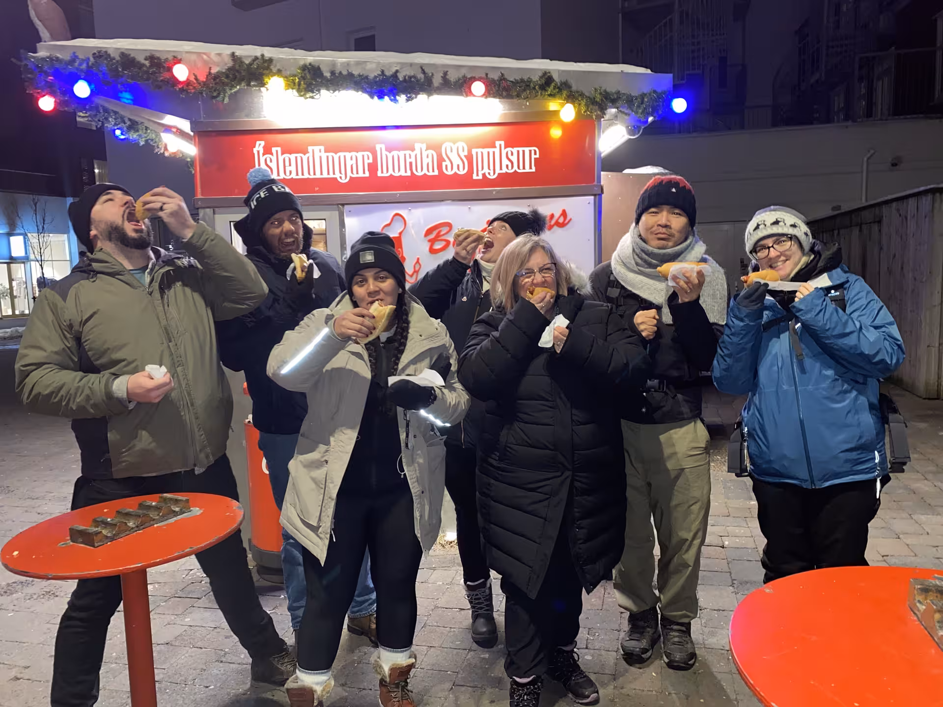 Group of tourists eating Icelandic hot dogs at Bæjarins Beztu Pylsur stand in Reykjavik at night