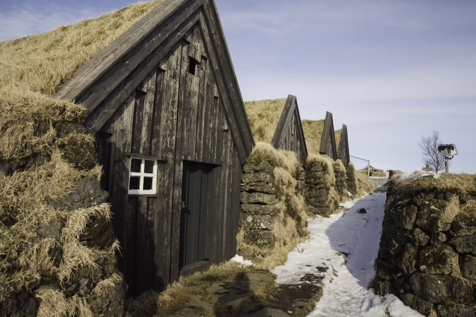 Historic Icelandic turf houses with grass roofs and snowy path evoking ancient witchcraft and Nordic magic traditions.