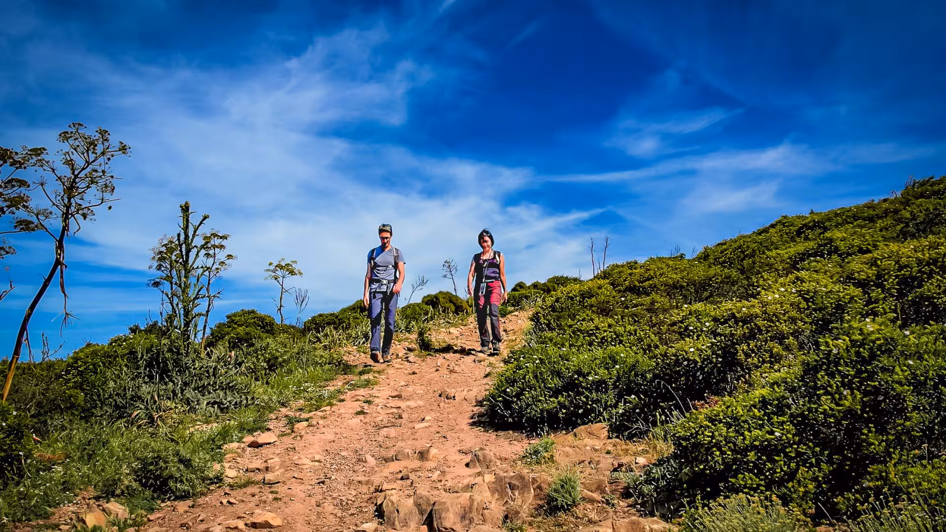 Hiking duo enjoying a scenic trail with lush greenery and clear blue skies on the Iglesias jeep tour adventure.