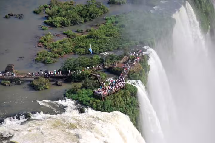 Visitors on a viewing platform at Iguazu Falls, surrounded by lush greenery and dramatic waterfalls.