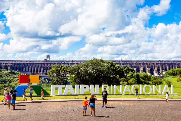 Visitors explore the Itaipu Dam sign under a vibrant sky during a private guided tour of Iguazu Falls.