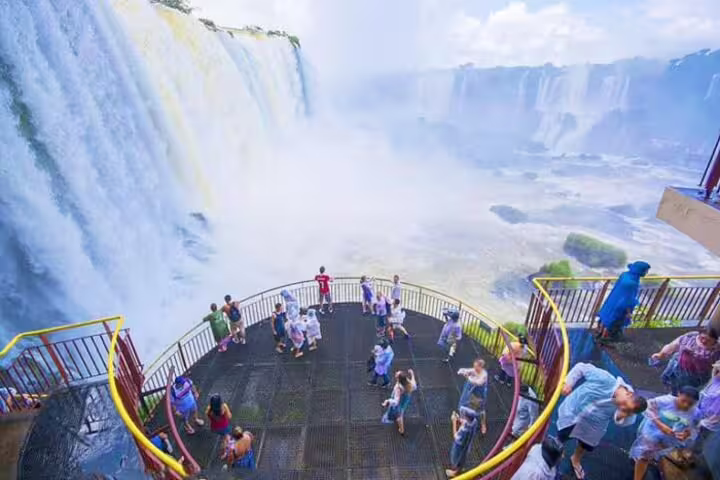 Tourists enjoy panoramic views from a platform at Iguazu Falls on the Argentine-Brazilian border, surrounded by mist.